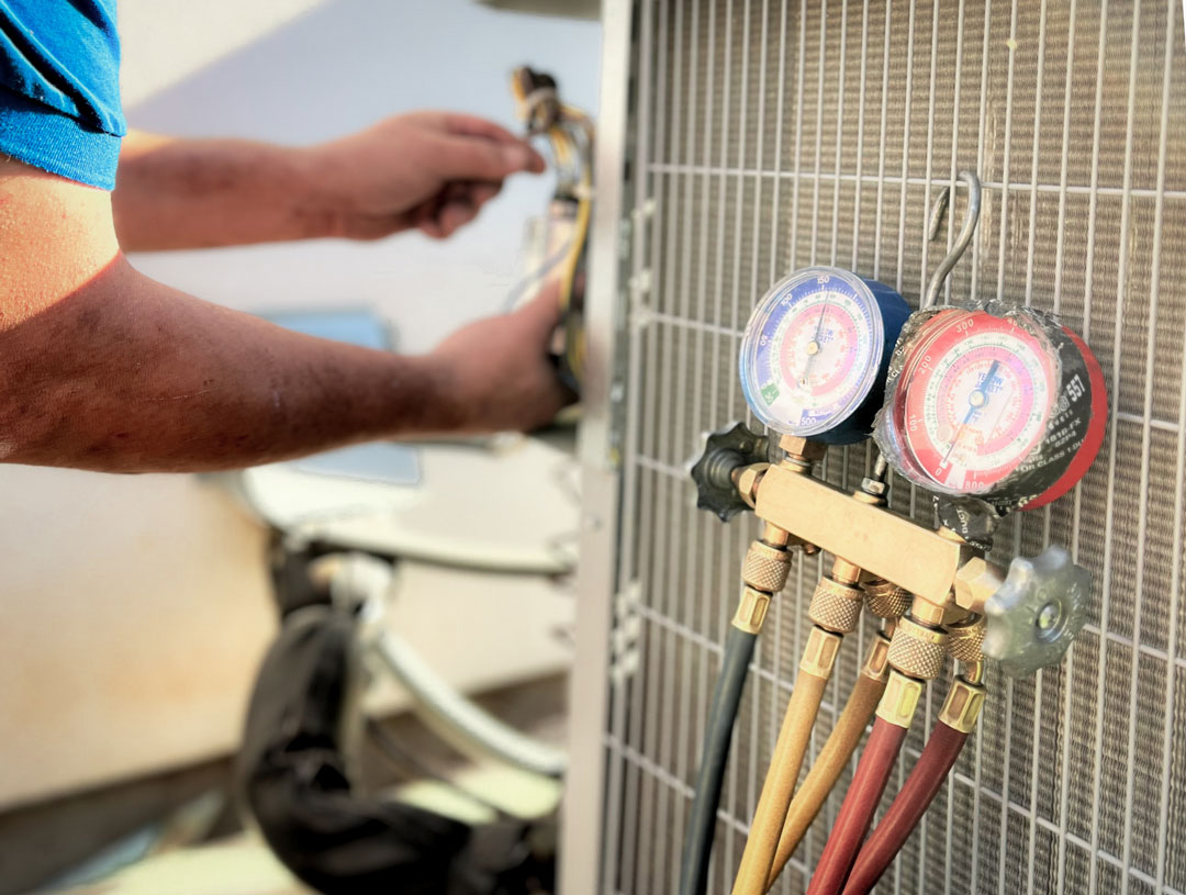 A technician works on an HVAC unit with gauges in the foreground.