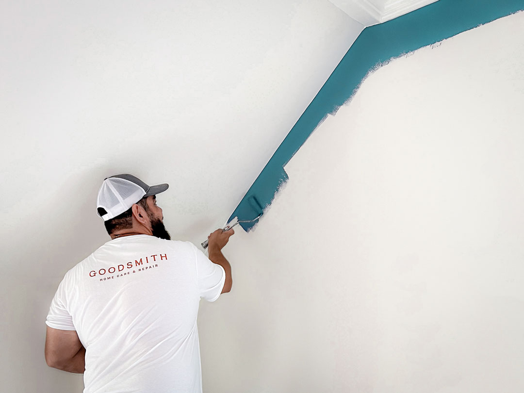 Man painting a teal border on an off-white wall.